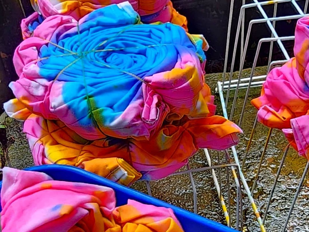 Fabric tied into bundles with string and dyed pink, orange and blue, draining on a rack