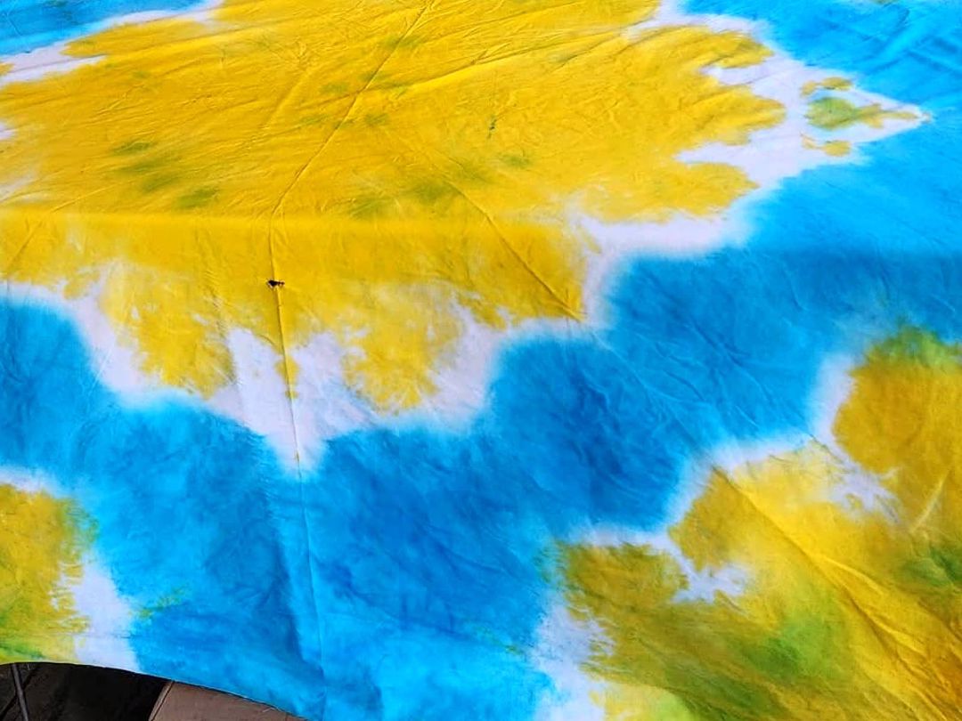 A large tie & dye sheet in yellow, blue and white, laid out flat to dry