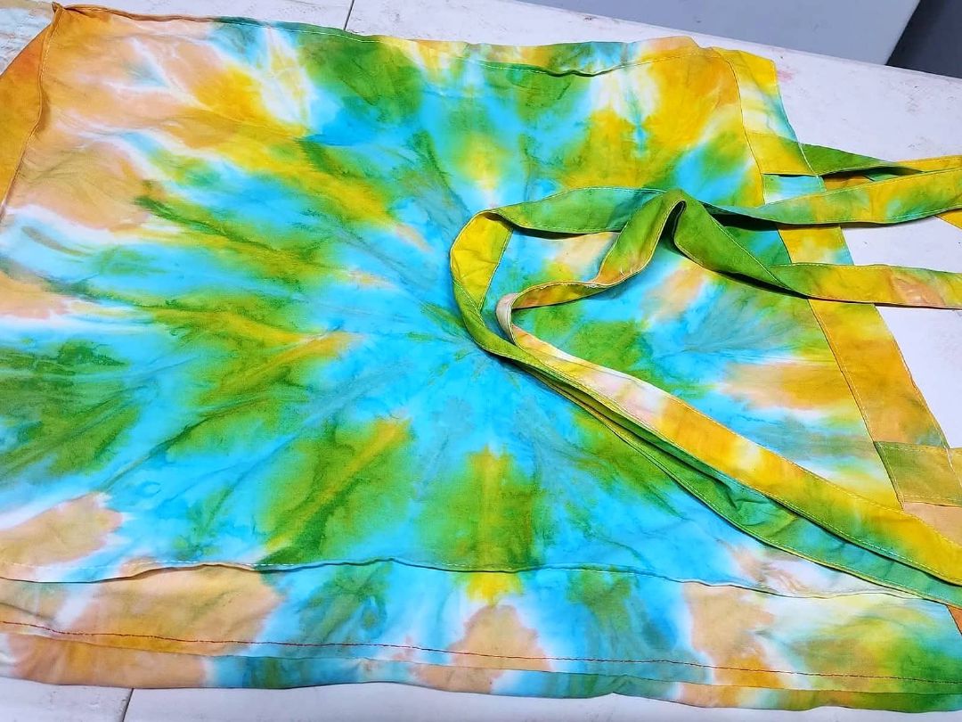 A finished tie & dye wrap in green, yellow and turquoise, laid flat with its fabric ties